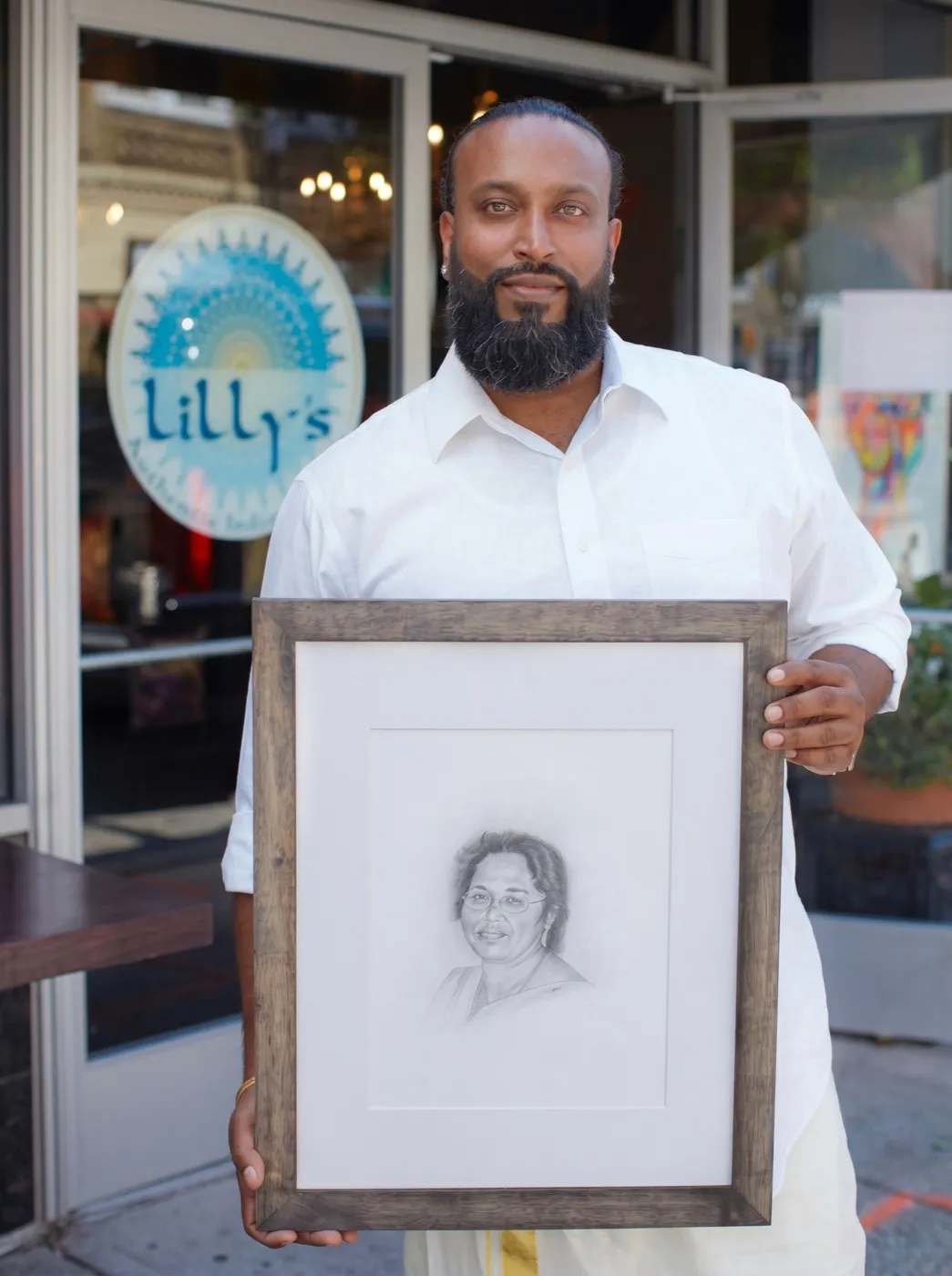 Jiji Thomas holding a framed portrait of his mother, Lilly Kutty Thomas